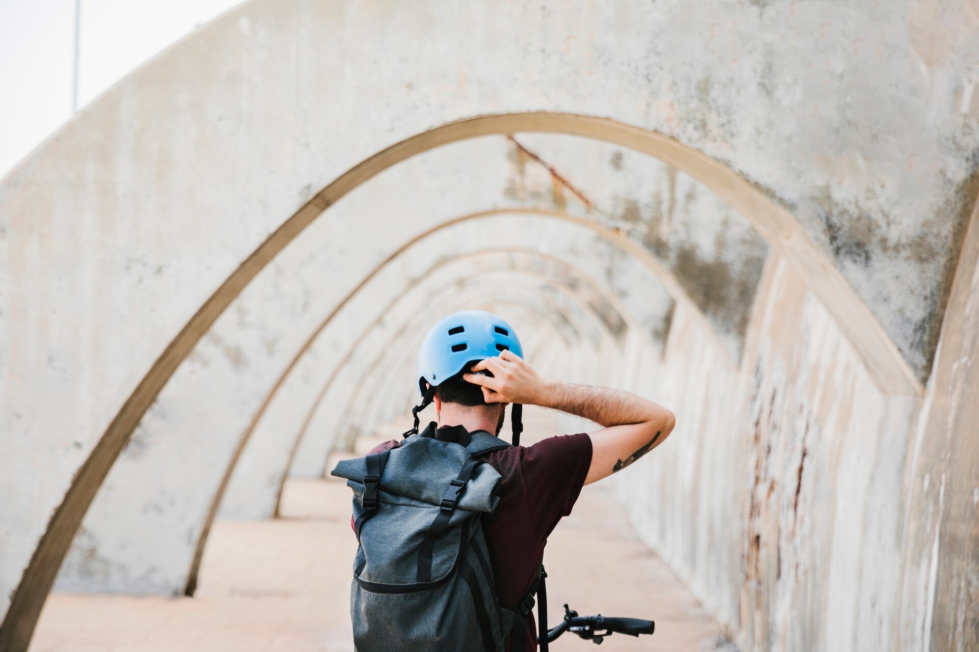 Cyklist med ryggsäck justerar en blå hjälm under betongvalv
