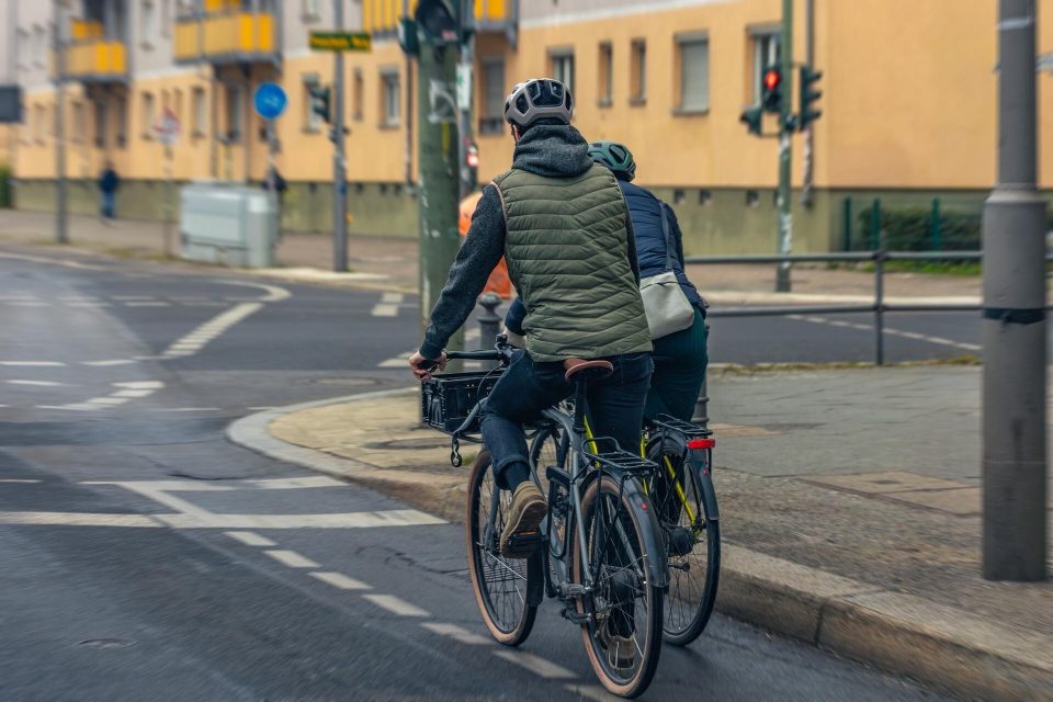 Två cyklister med hjälm vid ett övergångsställe i stan